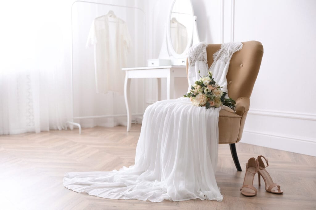 Elegant wedding dress, bouquet, and shoes on chair.