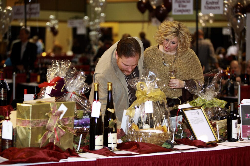 Couple browsing wine and gift baskets at event.